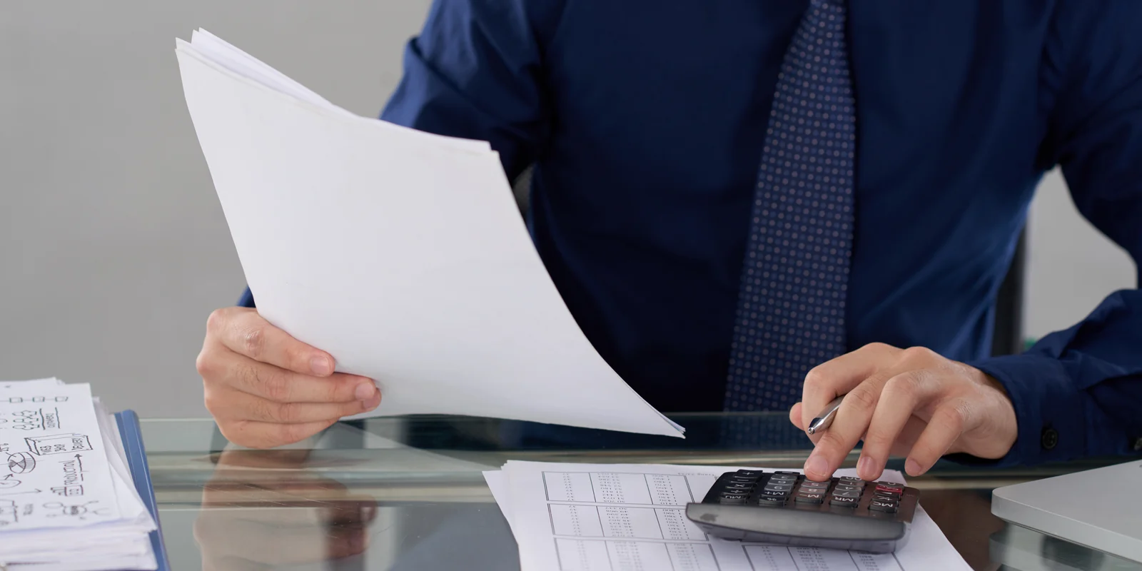 Profissional conferindo documentos fiscais com calculadora sobre a mesa